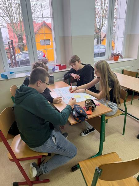 Na zdjęciu grupa uśmiechniętych uczniów wykonujących plakat tematyczny dotyczący projektu. 