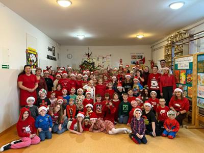 Na zdjęciu dzieci i nauczyciele świętujący Międzynarodowy Dzień Wolontariusza. Dzieci ubrane w mikołajkowe stroje. W tle choinka. 